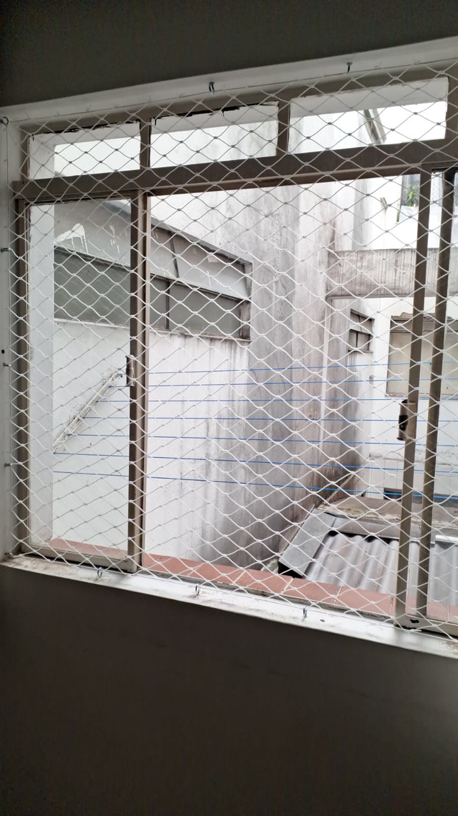 Rede de proteção branca fixada em janela com vista para área interna