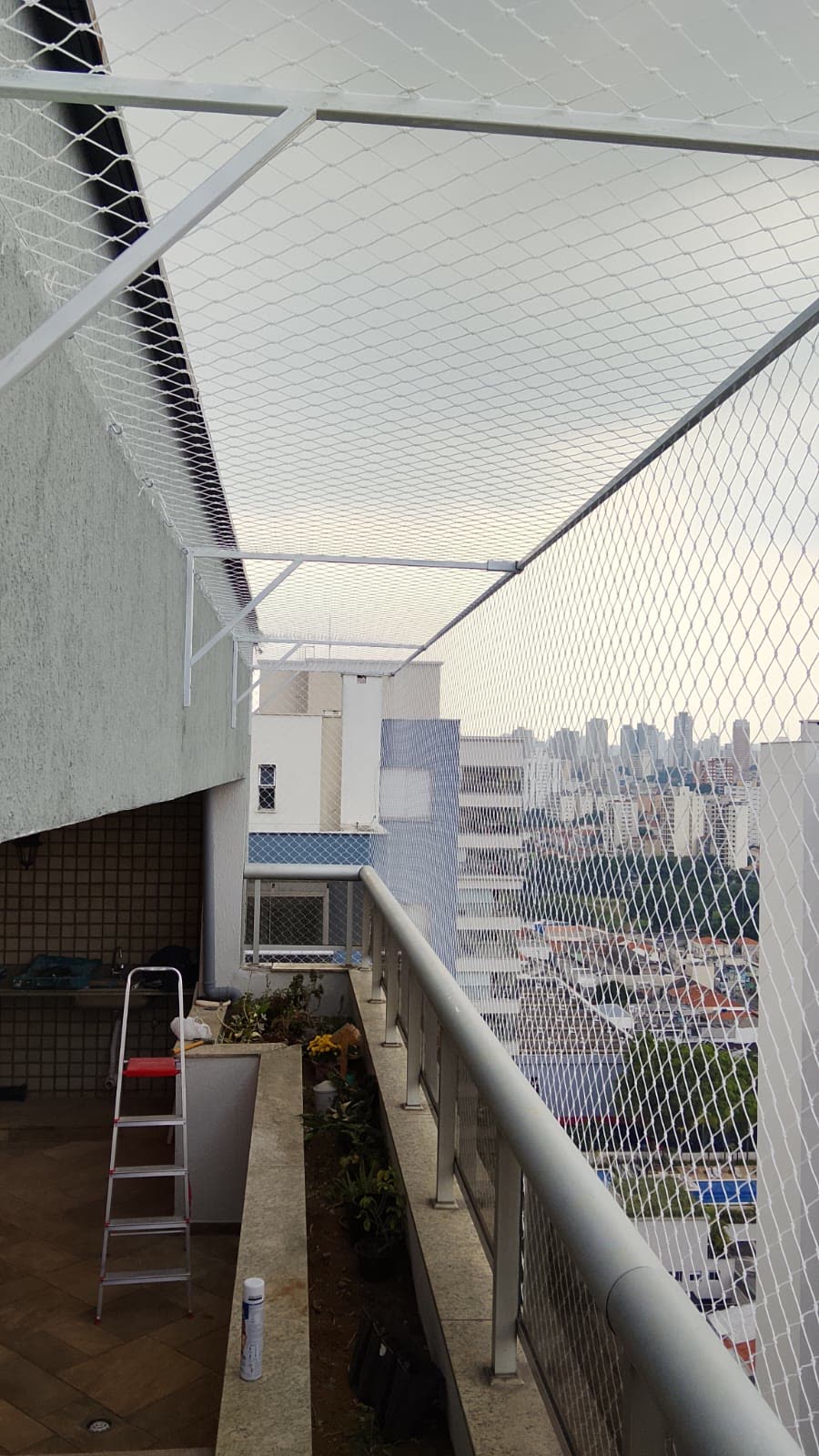 Cobertura de terraço fechada com rede de proteção branca e estrutura metálica